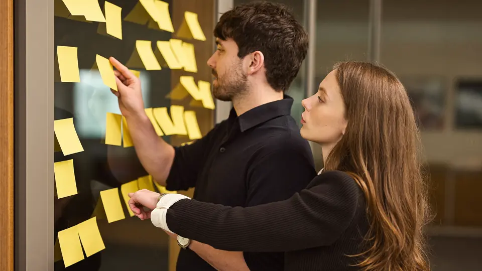 Dos compañeros organizando un plan sobre una pared de notas